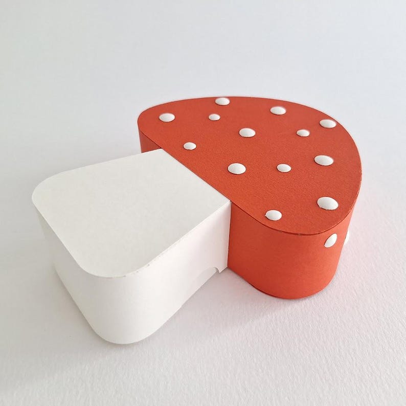 Pode incluir: Uma caixa de papel em forma de cogumelo vermelha e branca com bolinhas brancas. O cogumelo &eacute; feito de papel e tem um caule branco e um chap&eacute;u vermelho.