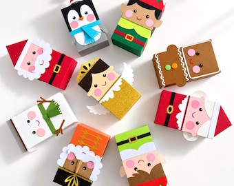 May include: A collection of eight rectangular paper gift boxes decorated as holiday characters including a penguin, elf, Santa Claus, gingerbread person, angel, snowman, and nutcracker, each featuring colorful cardstock cutouts and details.