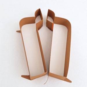 May include: Two brown paper boxes with a rectangular shape and a small flap on the top. The boxes are open and facing each other.