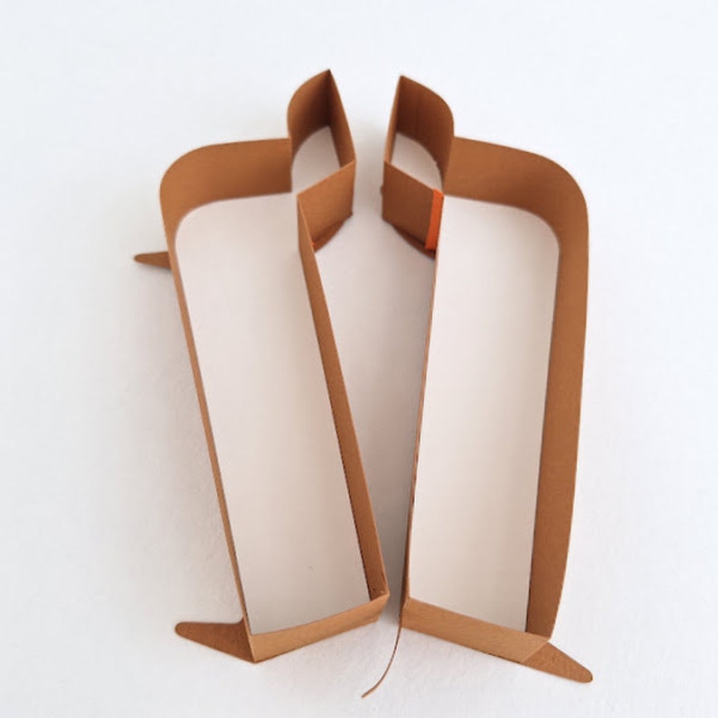 May include: Two brown paper boxes with a rectangular shape and a small flap on the top. The boxes are open and facing each other.