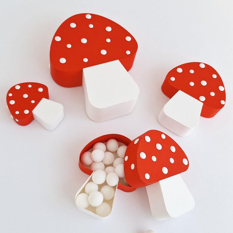 Pode incluir: Tr&ecirc;s caixas em forma de cogumelo vermelho e branco com bolinhas brancas. A caixa maior est&aacute; aberta e cheia de bolinhas de doces brancas. As caixas s&atilde;o feitas de papel.