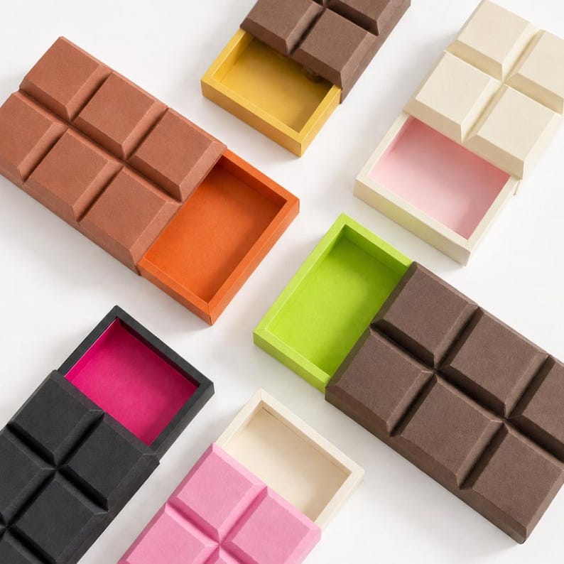May include: A collection of rectangular sliding storage boxes shaped like chocolate bars. Each box features a textured lid with a grid pattern and a contrasting interior color, including shades of brown, black, pink, cream, orange, and lime green.