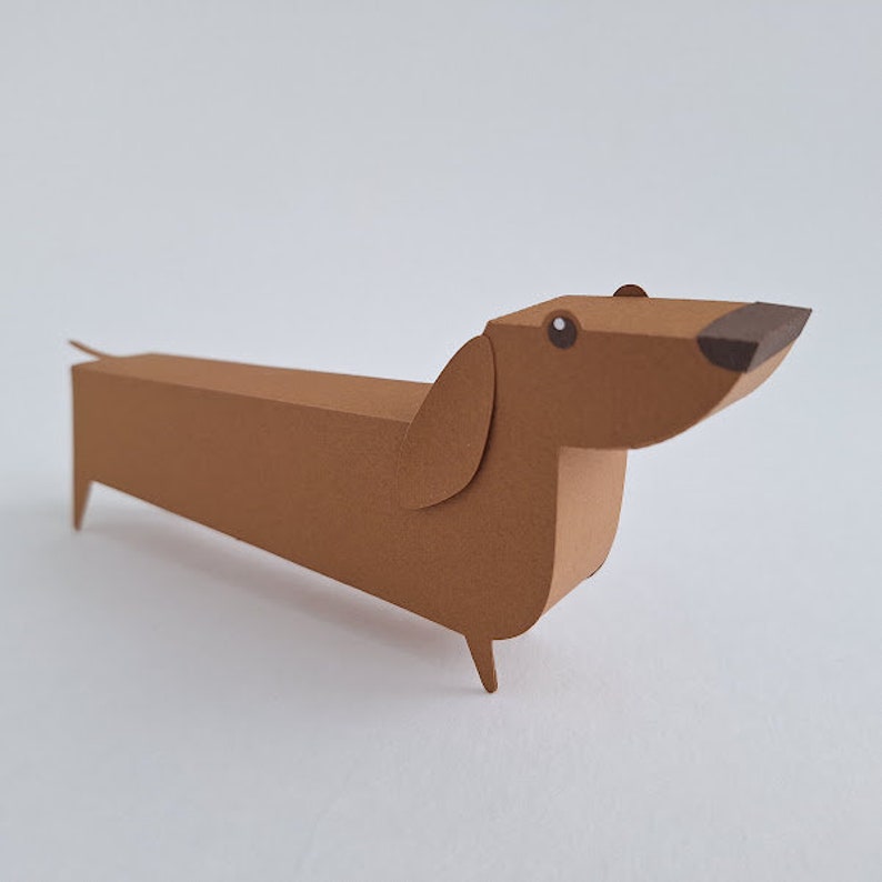 May include: A brown paper dachshund with black eyes and a black nose. The dachshund is made of paper and is a 3D model.