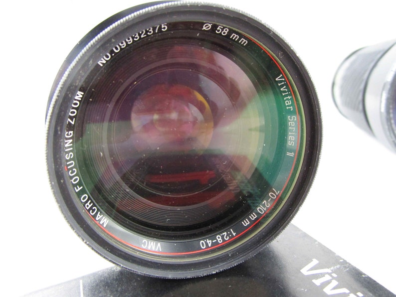 May include: A black Vivitar Series 11 70-210mm 1:2.8-4.0 macro focusing zoom lens with a 58mm filter thread. The lens has a red and white ring around the barrel.