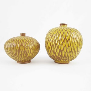 May include: Two yellow ceramic vases with a textured brown and yellow pattern. The vases are round and have a wide opening at the top.