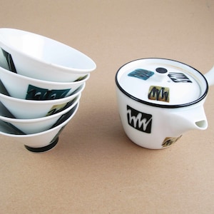May include: A set of five white ceramic teacups stacked on top of each other. The cups have a black rim and a design of black and green abstract shapes. A white ceramic teapot with a black rim and a design of black and green abstract shapes is also shown.