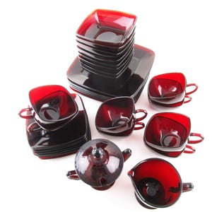 May include: A set of vintage ruby red glass dishes, including cups, saucers, and serving pieces. The square-shaped cups have small handles. The set includes a creamer, sugar bowl, and a stack of square plates. The glassware has a glossy finish.