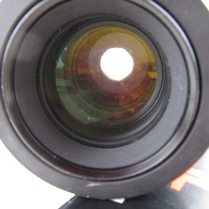 May include: Close-up of a black camera lens with a circular aperture. The lens has multiple layers of glass, visible through the aperture.