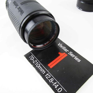 May include: A black Vivitar Series 70-210mm f2.8-f4.0 zoom lens with a black lens cap. The lens is sitting on a black and white instruction manual.
