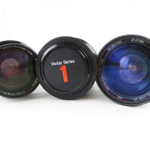 May include: Three black camera lenses with Vivitar Series 1 printed on the side. The lens on the left has a macro focusing zoom feature. The lens in the middle has a Vivitar Series 1 label with the number 1 printed in red. The lens on the right has a 67mm diameter and is a 28-105mm 1:2.8-38 lens.