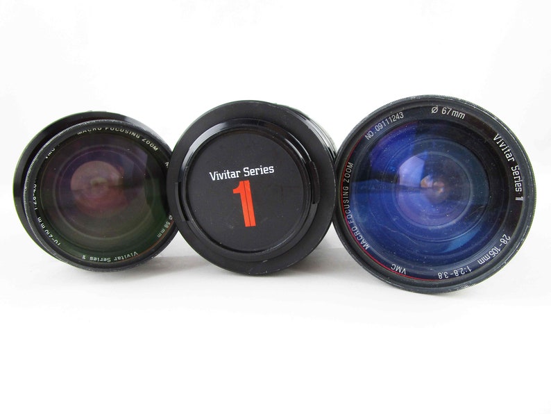 May include: Three black camera lenses with Vivitar Series 1 printed on the side. The lens on the left has a macro focusing zoom feature. The lens in the middle has a Vivitar Series 1 label with the number 1 printed in red. The lens on the right has a 67mm diameter and is a 28-105mm 1:2.8-38 lens.