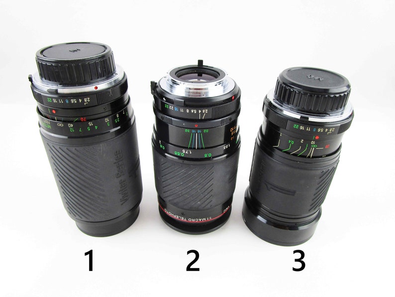 May include: Three black camera lenses with silver rings and markings. The lenses are labeled 1, 2, and 3. The lens labeled 2 has the text "77 MACRO TELEPHOTO" printed on it.