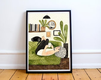 May include: Watercolor illustration in a black frame. The artwork depicts a person relaxing on a green polka-dot couch, holding a mug. A black cat rests nearby. The background includes a bookshelf, plants, and a mirror.