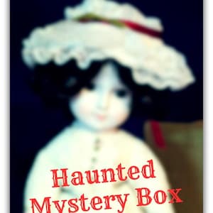 May include: A doll with dark hair wearing a white ruffled hat and a white dress, featuring the red text "Haunted Mystery Box" overlaid on the front of the image. The doll has a pale complexion and is set against a dark background.
