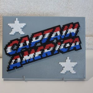 May include: A gray canvas with a red, white, and blue beaded design that says "CAPTAIN AMERICA" with two white beaded stars on the top and bottom of the design.