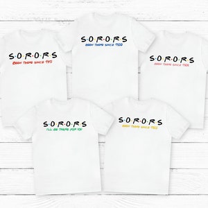 Könnte beinhalten: Fünf weiße T-Shirts mit dem Wort "SORORS" in Regenbogenfarben darauf gedruckt. Jedes Shirt hat einen anderen Spruch unter dem Wort, darunter "Been there since 1920", "Been there since 1911", "Been there since 1908", "I'll be there for you" und "Been there since 1922".