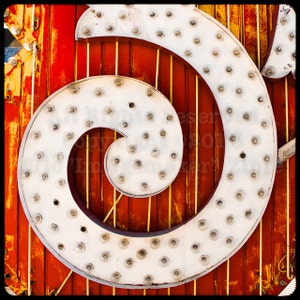 May include: A white, metal, spiral-shaped sign with a red and yellow background. The sign is made up of many small, round lights.