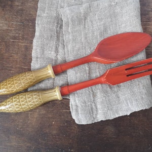 Puede incluir: Un juego de dos utensilios de cocina de madera, una cuchara roja y un tenedor rojo, con mangos de patrón marrón y amarillo.