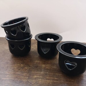 以下が含まれることがあります： ハート型の切り抜きのある黒いセラミック製のキャンドルホルダーが4つ。ホルダーは積み重ねられています。