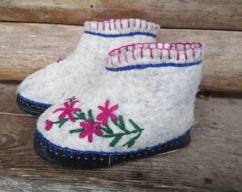 May include: A pair of gray felt slippers with embroidered pink flowers and green leaves. The slippers have a black rubber sole and a blue and white trim.