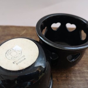 以下が含まれることがあります： ハート型の切り抜きのある黒いセラミック製のキャンドルホルダー2つ。1つのホルダーの底には、「Svenska Keramikk, Stengods, Sverige」というテキストが書かれた白いラベルがあります。