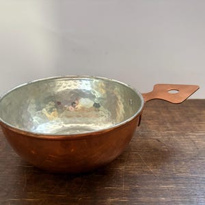 Peut inclure: Un bol rond en cuivre avec un extérieur martelé et un intérieur lisse de couleur argentée. Le bol présente une poignée plate et triangulaire s'étendant d'un côté, comprenant un trou circulaire pour le suspendre ou le ranger facilement.