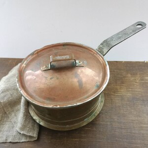 Può includere: Una pentola di rame vintage con coperchio e manico in metallo. La pentola ha un'etichetta che recita "G.B. SYSTRON, CHICAGO, ILL."