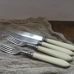 Peut inclure: Trois fourchettes en argent et un couteau en argent avec des manches en ivoire. Les couverts sont disposés sur un tissu en lin beige.