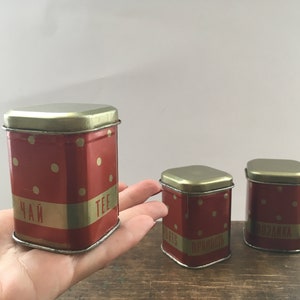 Peut inclure: Trois boîtes carrées en étain rouge et or avec des pois blancs. Les boîtes portent des inscriptions dorées qui disent "Чай" (thé), "TEE" (thé) et "ВЗЯНКА" (un type de pain russe).