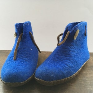 Könnte beinhalten: Ein Paar blaue Filzpantoffeln mit braunen Lederschnallen und einem braunen Lederbesatz um die Sohle.
