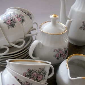 Könnte beinhalten: Ein Vintage-Porzellan-Tee-Set mit einem floralen Muster in Rosa- und Schwarztönen. Das Set beinhaltet eine Teekanne, eine Zuckerdose, eine Milchkännchen und vier Teetassen mit Untertassen.