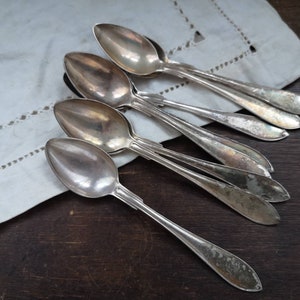 May include: A set of six silver spoons with ornate handles. The spoons are arranged in a fan shape on a white cloth.