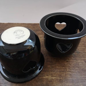 以下が含まれることがあります： ハート型の切り抜きが施された黒いセラミック製のキャンドルホルダー2つ。ホルダーは滑らかで光沢のあるセラミック製で、シンプルでエレガントなデザインです。