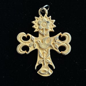 Peut inclure: Pendentif doré en forme de croix. La croix présente une fleur, une colombe et des détails floraux et en volutes. Le pendentif a une petite boucle en haut pour une chaîne.