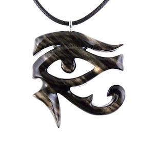A wooden pendant in the shape of the Eye of Horus, a symbol of protection and good health in ancient Egyptian culture. The pendant is black with light brown streaks and is hanging from a black cord.