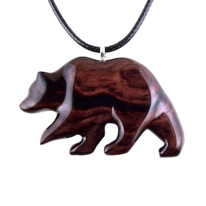 A wooden bear pendant necklace. The pendant is carved from dark reddish-brown wood with a visible grain pattern. The bear is depicted in a walking pose and is attached to a black cord necklace with a silver-colored clasp.