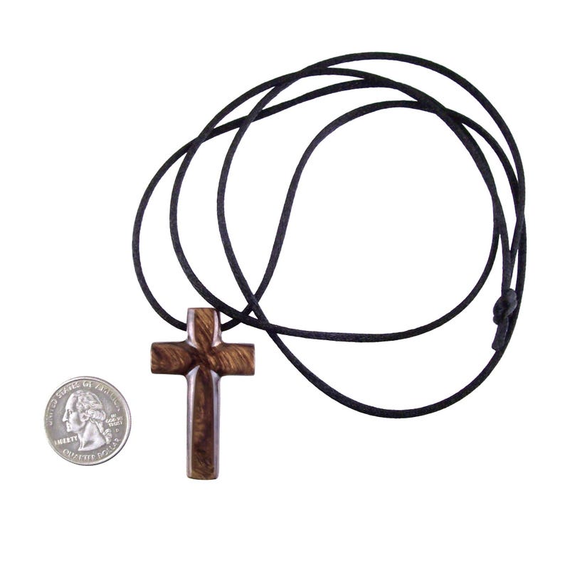 A dark brown wooden cross necklace on a black cord. The cross is carved with visible wood grain, and the cord is simple.  The pendant is shown next to a US quarter for scale. This religious jewelry is perfect for everyday wear.