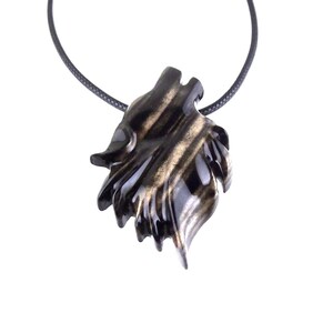 A black with brown streaks wooden pendant shaped like a wolf's head, hanging from a black cord necklace.