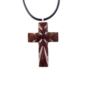 A dark brown wooden cross pendant necklace. The cross features a geometric, faceted design with a high-polished finish. It hangs from a simple black cord necklace. The pendant is intricately carved, showcasing the wood's natural grain and rich color. This religious jewelry piece is perfect for everyday wear or special occasions.