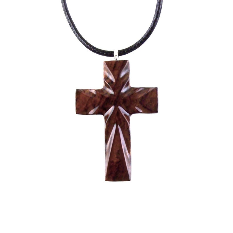 A dark brown wooden cross pendant necklace. The cross features a geometric, faceted design with a high-polished finish. It hangs from a simple black cord necklace. The pendant is intricately carved, showcasing the wood's natural grain and rich color. This religious jewelry piece is perfect for everyday wear or special occasions.
