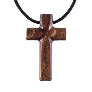 A dark brown wooden cross pendant necklace. The cross features a unique wood grain pattern and is suspended from a simple black cord.  The pendant is intricately carved with visible wood grain detail. This religious jewelry piece is perfect for everyday wear.
