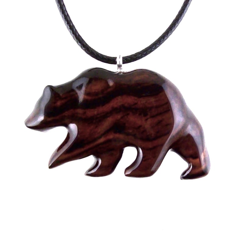 A wooden bear pendant necklace. The pendant is carved from dark reddish-brown wood with a visible grain pattern. The bear is depicted in a walking pose and is attached to a black cord necklace with a silver-colored clasp.