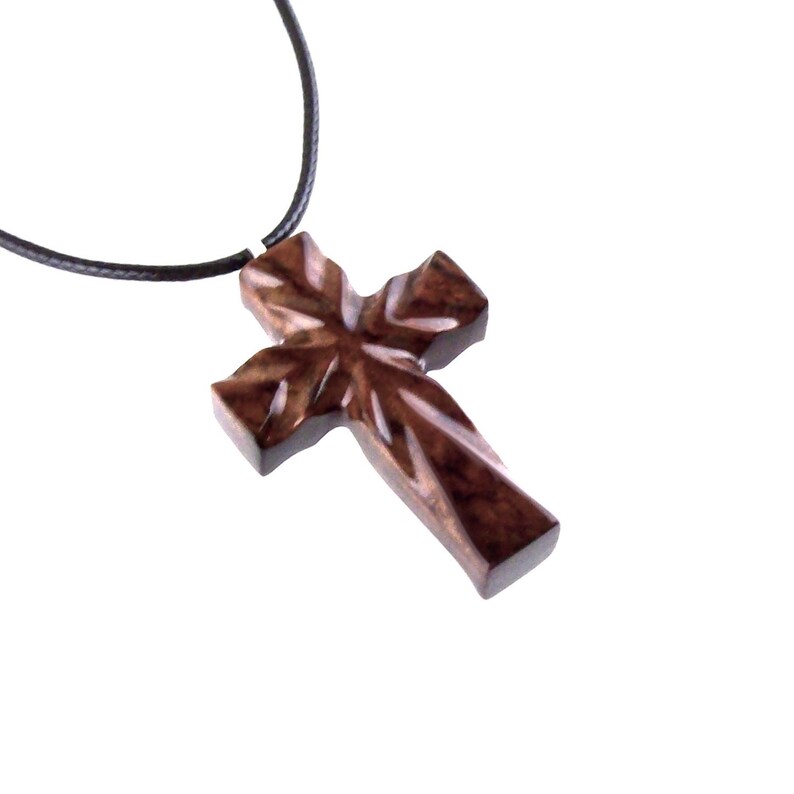 A dark brown wooden cross pendant necklace on a black cord. The cross has a unique wood grain pattern and is intricately carved.  The pendant is simple yet elegant, suitable for religious or fashion jewelry. The necklace is approximately 18 inches long.