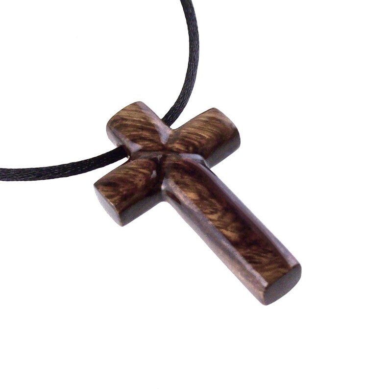A dark brown wooden cross necklace pendant hangs from a black cord. The cross has a detailed, carved wood grain texture.  The pendant is simple yet elegant, suitable for religious or spiritual jewelry. The wood's rich color and the smooth, polished finish are clearly visible.