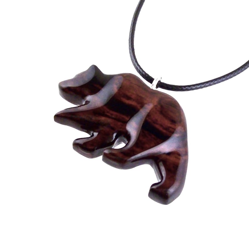A wooden bear pendant with a dark reddish-brown finish and a black cord necklace. The bear is carved in a stylized form, with visible wood grain. The pendant is suspended from a black cord.