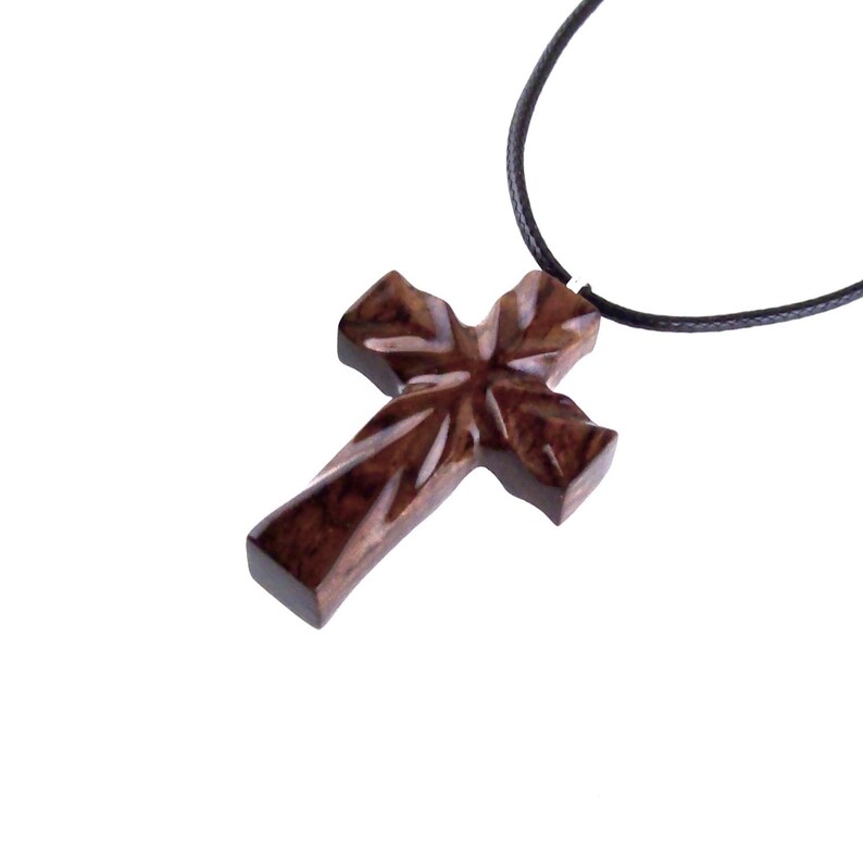 A dark brown wooden cross pendant necklace on a black cord. The cross has a unique wood grain pattern and is intricately carved.  The pendant is simple yet elegant, suitable for religious or fashion jewelry.