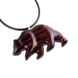 A reddish-brown wooden bear pendant on a black cord necklace. The bear pendant is carved with visible wood grain and has a glossy finish. The necklace is displayed against a white background.