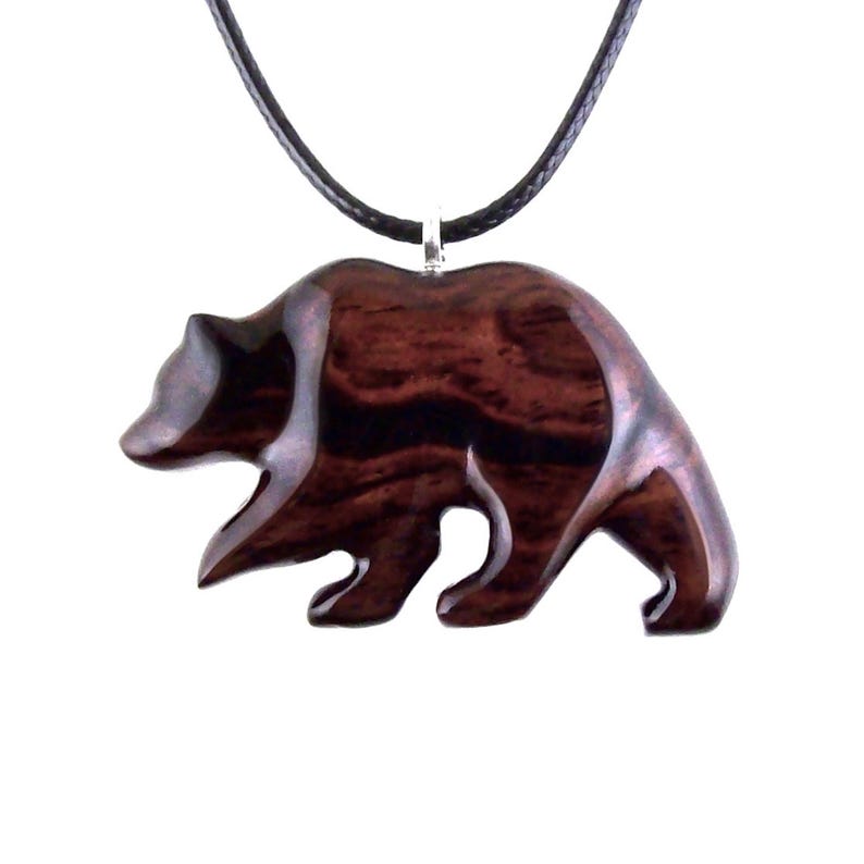 A wooden bear pendant necklace. The pendant is carved from dark reddish-brown wood with a visible grain pattern. The bear is depicted in a walking pose and is attached to a black cord necklace with a silver-colored clasp.