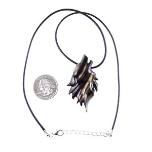 A wooden wolf head pendant necklace in black with brown streaks wood grain with glossy finish. The pendant is hanging from a black cord and a silver chain.