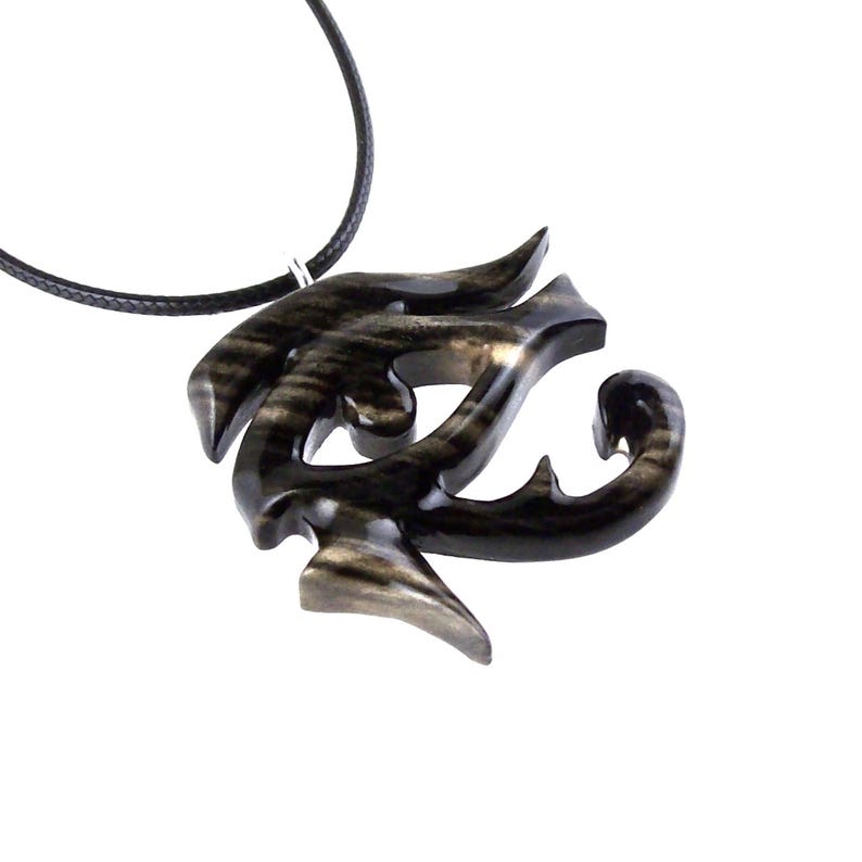 A wooden pendant necklace with a black eye symbol. The pendant is intricately carved and has a black cord.